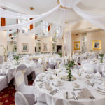 The Ballroom on the Park at Mercure Leeds Parkway Hotel set up for a wedding breakfast, white drapes on ceiling