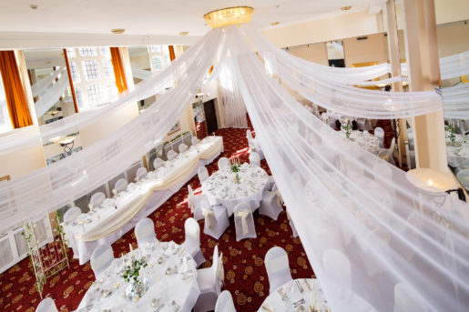 The Ballroom on the Park at Mercure Leeds Parkway Hotel set up for a wedding breakfast, white drapes on ceiling