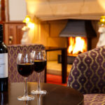 Cosy armchairs, two glasses of red wine next to a roaring fire