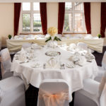 The Park Side Room at Mercure Leeds Parkway Hotel set up for a wedding breakfast, peach sashes, white tablecloths and yellow flowers