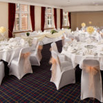 The Park Side Room at Mercure Leeds Parkway Hotel set up for a wedding breakfast, peach sashes, white tablecloths and yellow flowers