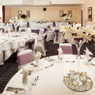 The Park Side Room at Mercure Leeds Parkway Hotel set up for a wedding breakfast, purple sashes, white tablecloths and purple flowers
