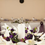 White candle with purple flowers centrepiece in the Park Side Room at Mercure Leeds Parkway Hotel, wedding breakfast, top table in background