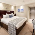Privilege bedroom at Mercure Leeds Parkway Hotel, blue velvet armchair beside bed, blue artwork on walls and white desk
