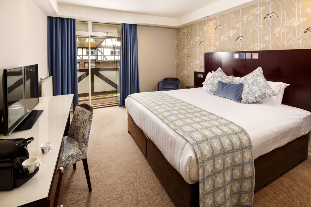Privilege bedroom at Mercure Leeds Parkway Hotel, blue velvet cushion on bed, blue floor length curtain and white desk